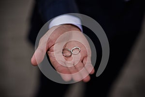 Groom holding wedding rings in hand. Two wedding rings on the floor with contrast wedding rings on floor, on ground, on piano, in