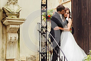 Groom holds bide`s face tender standing with her on the stairs o photo