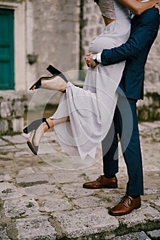 Groom holds bride in his arms while standing on the paving stones in the courtyard of the house