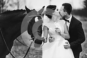 Groom holds bride tender standing behind a horse