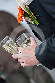 The groom holds a glass or flute of champagne on the background of the friends on nature at the wedding ceremony. Close