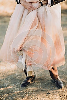 The groom holds on hand a bride in her unusual pink dress. Shoes close-up