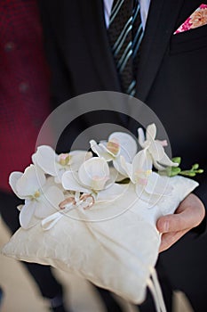 The groom holds in his hands a pillow on which lie wedding rings