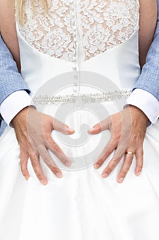 Groom holds his hands in the shape of a heart on the back of the bride in a white dress