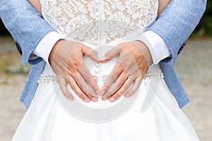 Groom holds his hands in the shape of a heart on the back of the bride in a white dress