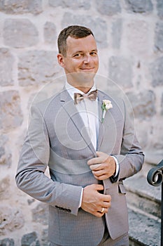 Groom holds the lapels of his jacket with his hands and stands on the stone stairs photo