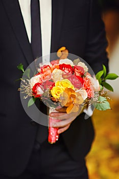 Groom holds a red bouquet of little roses