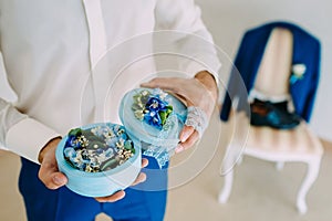Groom holds a round box with Wedding rings with blue flowers. Artwork. Soft focus, Close-up