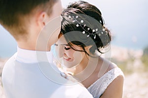 The groom hugs the bride and kisses on the forehead, the bride smiles, close-up