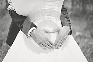The groom hugs the bride by the waist and folds his hands in the shape of a heart
