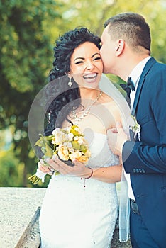 Groom kiss happy bride with bouquet. Woman and man smile on wedding day. Wedding couple in love. Newlywed couple on
