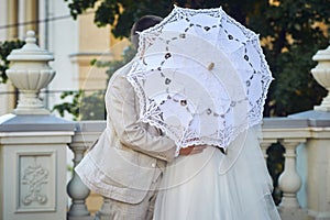 groom kisses the bride  covered with a white lace umbrella. wedding scene on the balcony