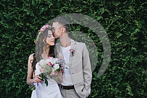 groom kissing and embracing attractive bride in wedding dress with wreath