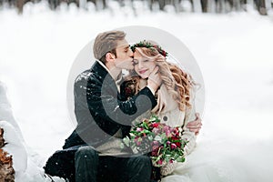 Groom is kissing his bride on the temple on the white snow background. Artwork. Selective focus on the bouquet