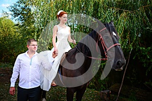 The groom leads the horse by the bridle. Bride sits in the saddl