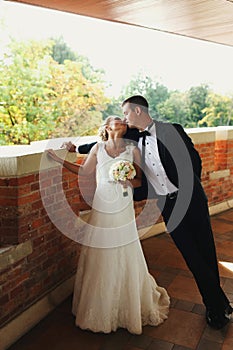 Groom leans over a bride and kiss her standing on the balcony