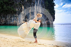 Groom lifts blonde curly bride in fluffy dress on beach