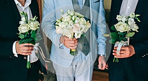 Groom in light blue suit is holding wedding bouquet. Best man friends are standing nearby.  Elegant photo