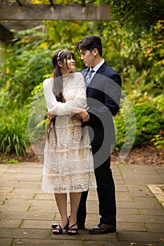 Groom in navy suit hugging bride outdoors under vines