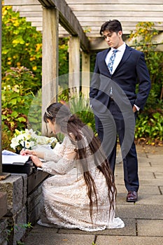 Groom in navy suit watching bride sign wedding certificate outdoors