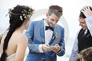 Groom occupied with phone at beach wedding ceremony photo