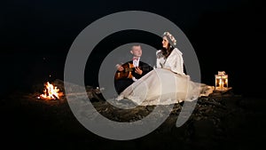 Groom playing guitar in the night at campfire