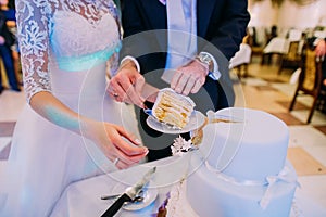 Groom puts the first piece of the wed cake on the plate. Close-up view of the hands.