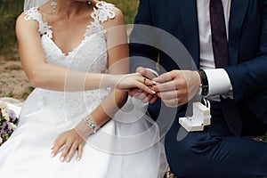 The groom puts a gold engagement ring on the finger of his bride