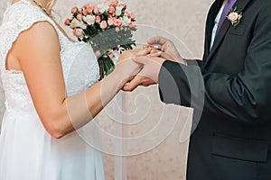 Groom puts a gold wedding ring on the bride`s finger