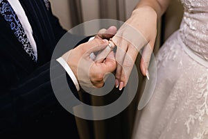 The groom puts a gold wedding ring on the bride`s finger close-up