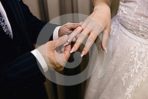 The groom puts a gold wedding ring on the bride`s finger close-up