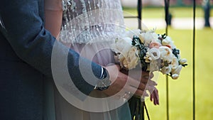 The groom puts his hands on the abdomen of the bride. The bride holds flowers in her hands. Close-up only hands