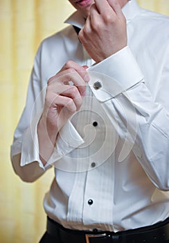 A groom putting on cuff-links as he gets dressed