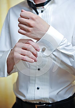 A groom putting on cuff-links as he gets dressed