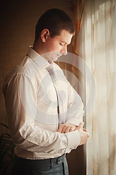 Groom putting on cuff-links as he gets dressed