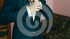 A groom putting on cuff-links as he gets dressed in formal wear .Groom's suit