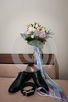 Groom& x27;s accessories. Black leather men& x27;s shoes, bride& x27;s bouquet, black leather belt on a brown background