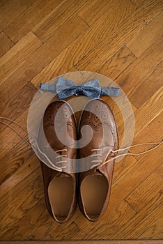 The groom`s accessories. Blue bow tie and a brown leather shoes on a wooden background.