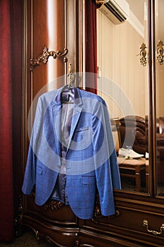 The groom`s blue jacket on a hanger on a vintage wardrobe. Groom`s morning, wedding details, preparation for the wedding ceremon