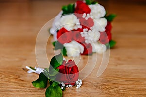 The groom`s boutonniere of red roses and the bride`s bouquet of red and white roses