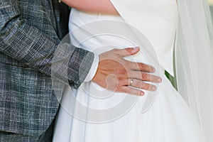 Groom`s hand with the wedding ring lies on the bride`s waist