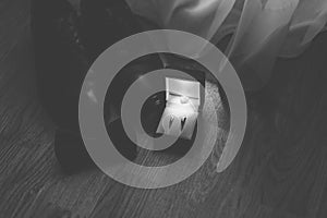 The groom's new black shoes on the floor near a white curtain with a butterfly and wedding rings on the wedding day