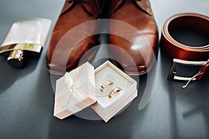 Groom`s wedding day accessories. Brown leather shoes, belt, perfume, golden rings. Male fashion