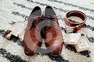 Groom`s wedding day accessories. Brown leather shoes, belt, perfume, golden rings. Male fashion