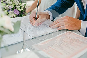 The groom signs the marriage registration documents. Young couple signing wedding documents.