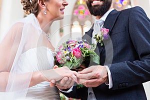 Groom slipping ring on finger of bride at wedding