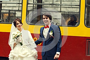 Groom smiles sincerely standing with a bride behind a tram photo