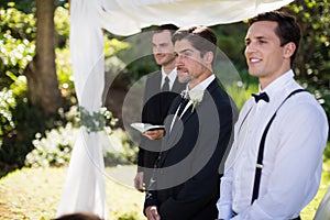 Groom standing with waiter and groomsman in park photo