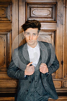 Groom stands with his hands on the lapels of his jacket against the background of a wooden wall. Lake Como