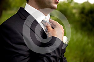 The groom in a suit, corrects a tie with his hand.